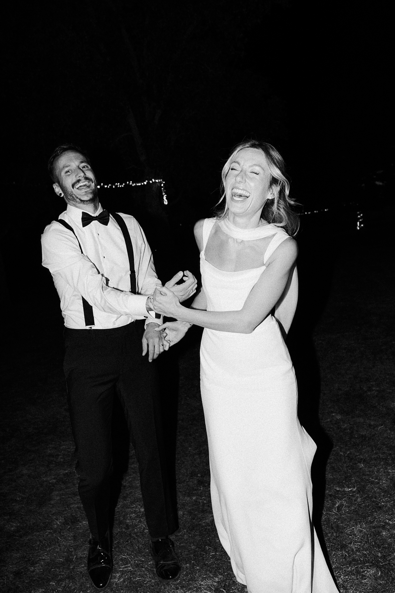 A bride and groom laugh joyfully during their wedding reception at night.